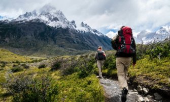 A hiker walking on a trail toward snow-capped mountains