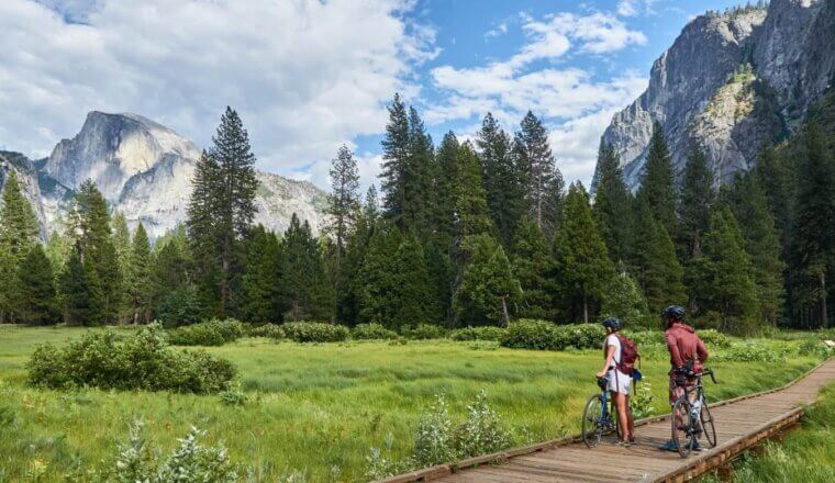 Two people on bikes stop and admire the landscape of forests and mountains at Yosemite Park in the United States