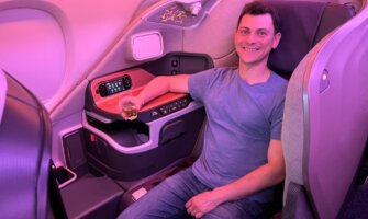 Travel blogger Nomadic Matt holding a glass of wine while sitting on an airplane in first class
