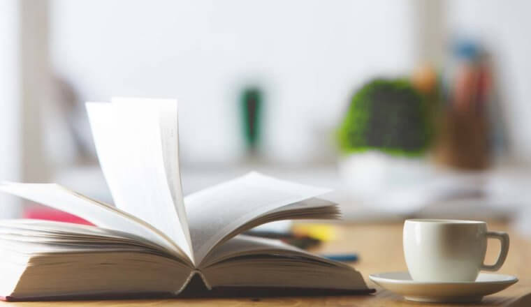 A book and a cup of tea on a desk in a well-lit office room