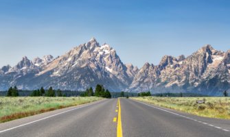 The open road on a sunny day in Wyoming, USA with mountains in the background