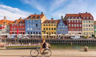 The colorful buildings of Copenhagen along the water as someone cycles by