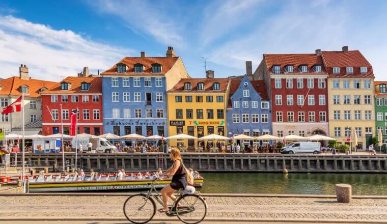 The colorful buildings of Copenhagen along the water as someone cycles by