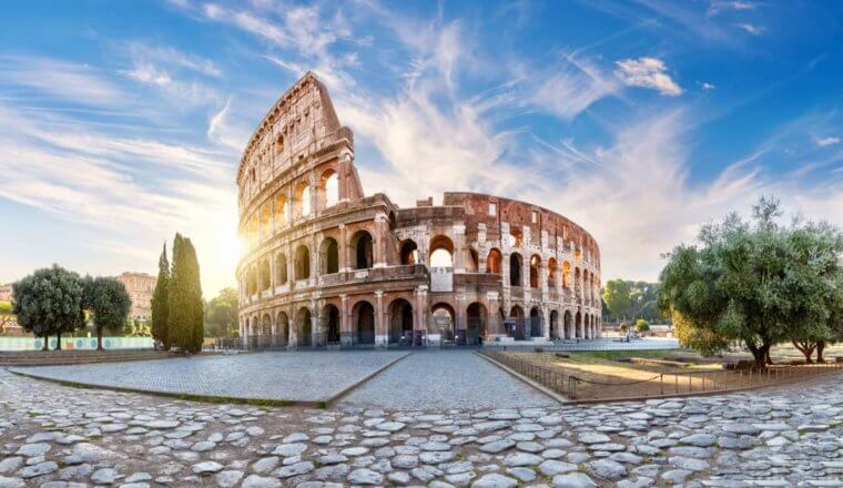 The massive colloseum in Rome, italy with the bright sun in the background on a sunny day