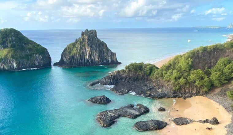 Panoramic view of a beach and two large rock formations rising out of the turquoise waters of Fernando de Noronha, Brazil