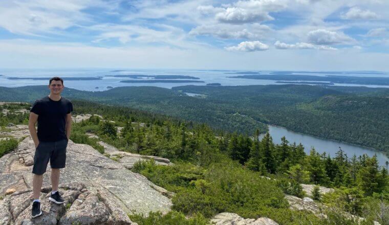 Matt standing on top of a mountain with a lush archipelago behind him in Maine, USA