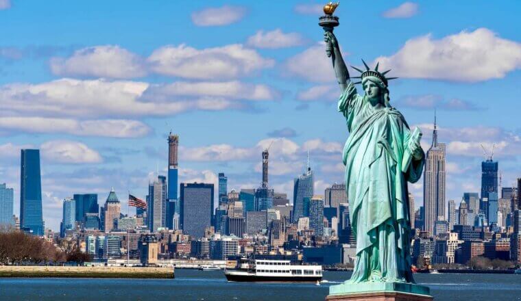 The iconic Statue of Liberty with NYC in the background on a sunny day with blue skies