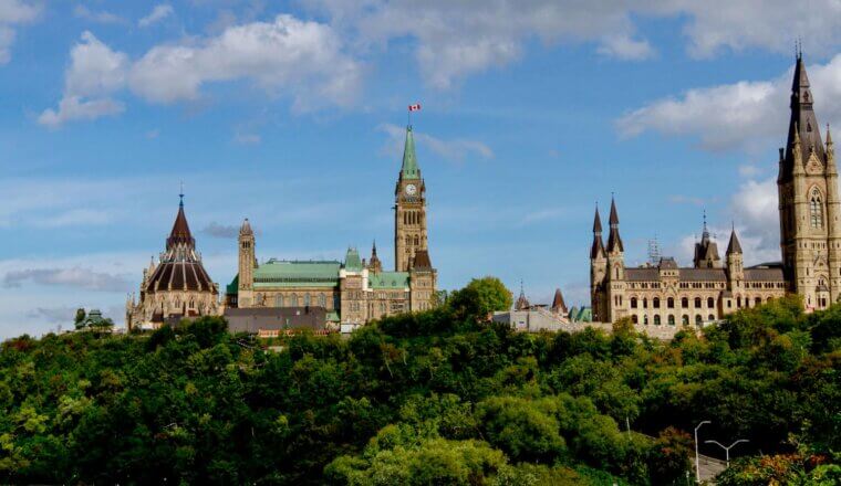 A view over the skyline of Ottawa, Canada, featuring the parliament buildings surrounded by lush green trees in summer