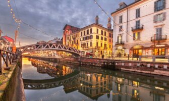 The picturesque and historic canals of the Navigli neighborhood with string lights hung over them in the twilight of the evening in Milan, Italy