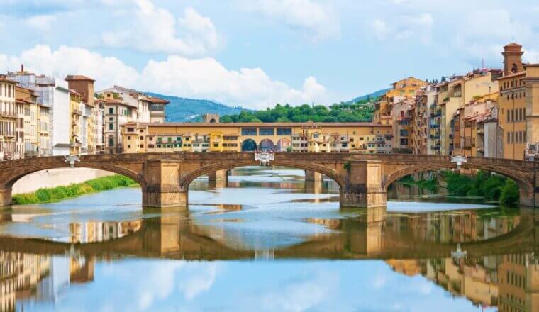 Panoramic of Ponte Vecchio stretching across the Arno River in Florence Italy, with both banks of the river as well as the bridge lined with yellow buildings