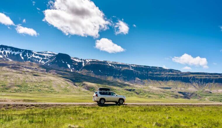 A 4x4 car parked on the side of the road in beautiful, sunny Iceland with mountains in the background