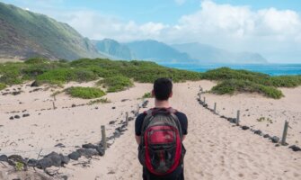 Nomadic Matt wearing a backpack while walking along a beach in Hawaii