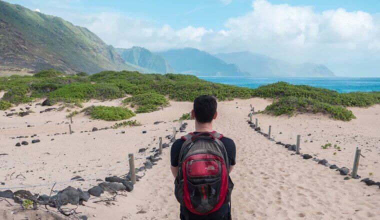 Nomadic Matt wearing a backpack while walking along a beach in Hawaii